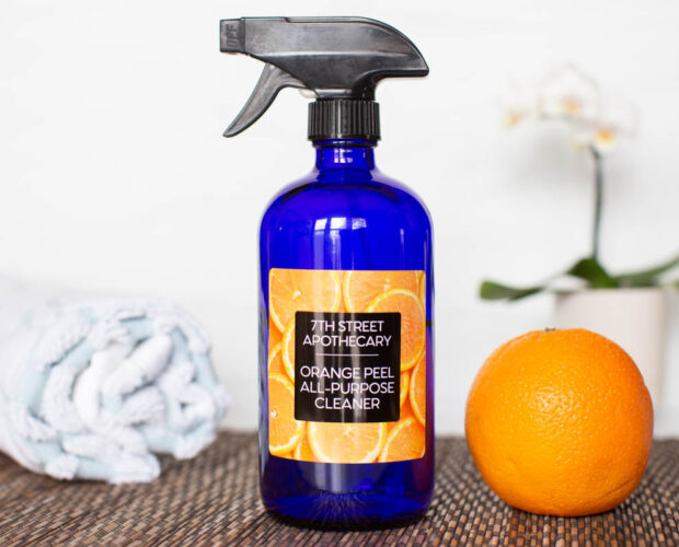 Homemade Orange Peel Cleaner in a blue bottle with a glossy orange personalized label